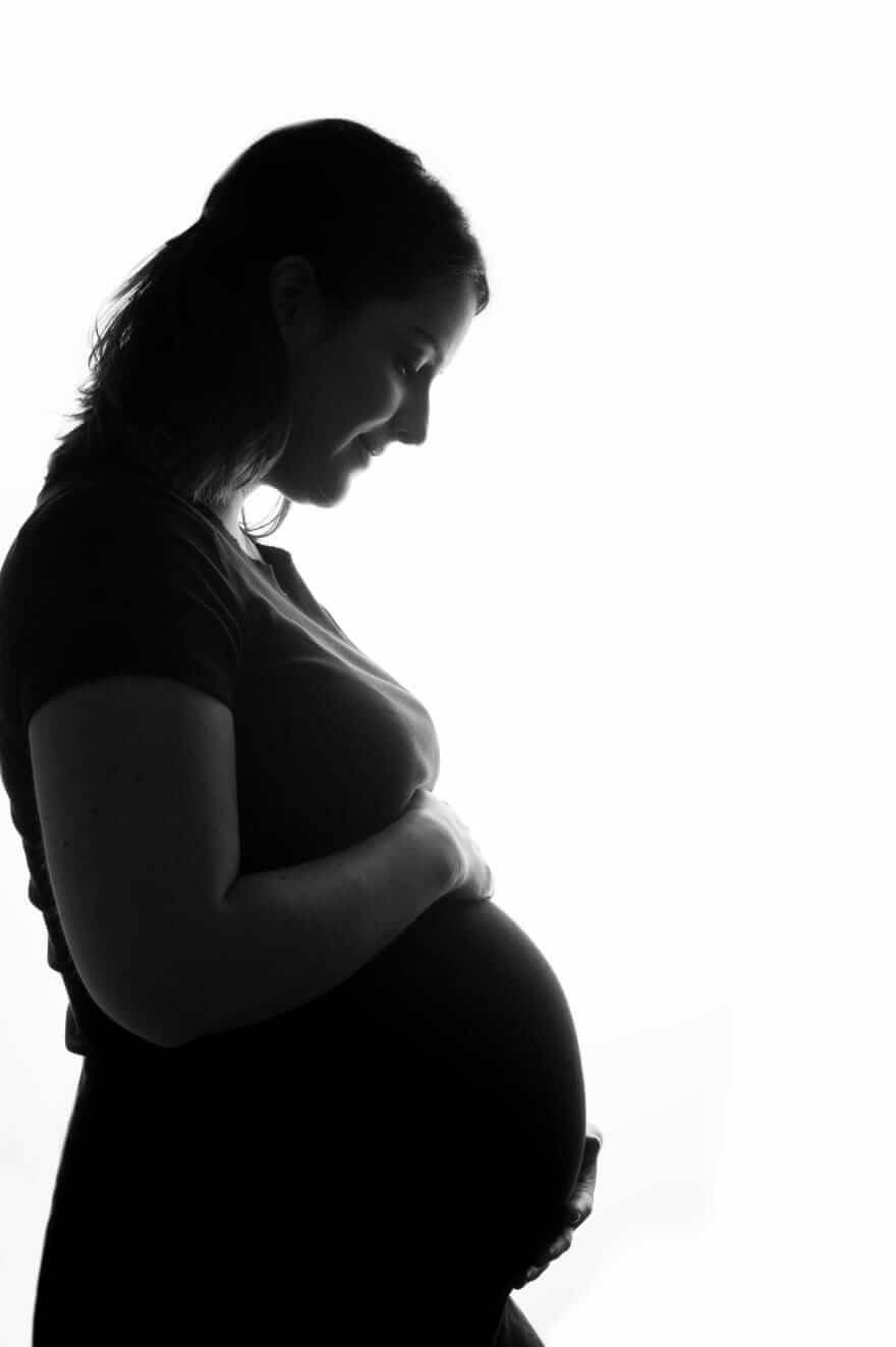 Silhueta de uma gestante de perfil, com as mãos apoiadas na barriga