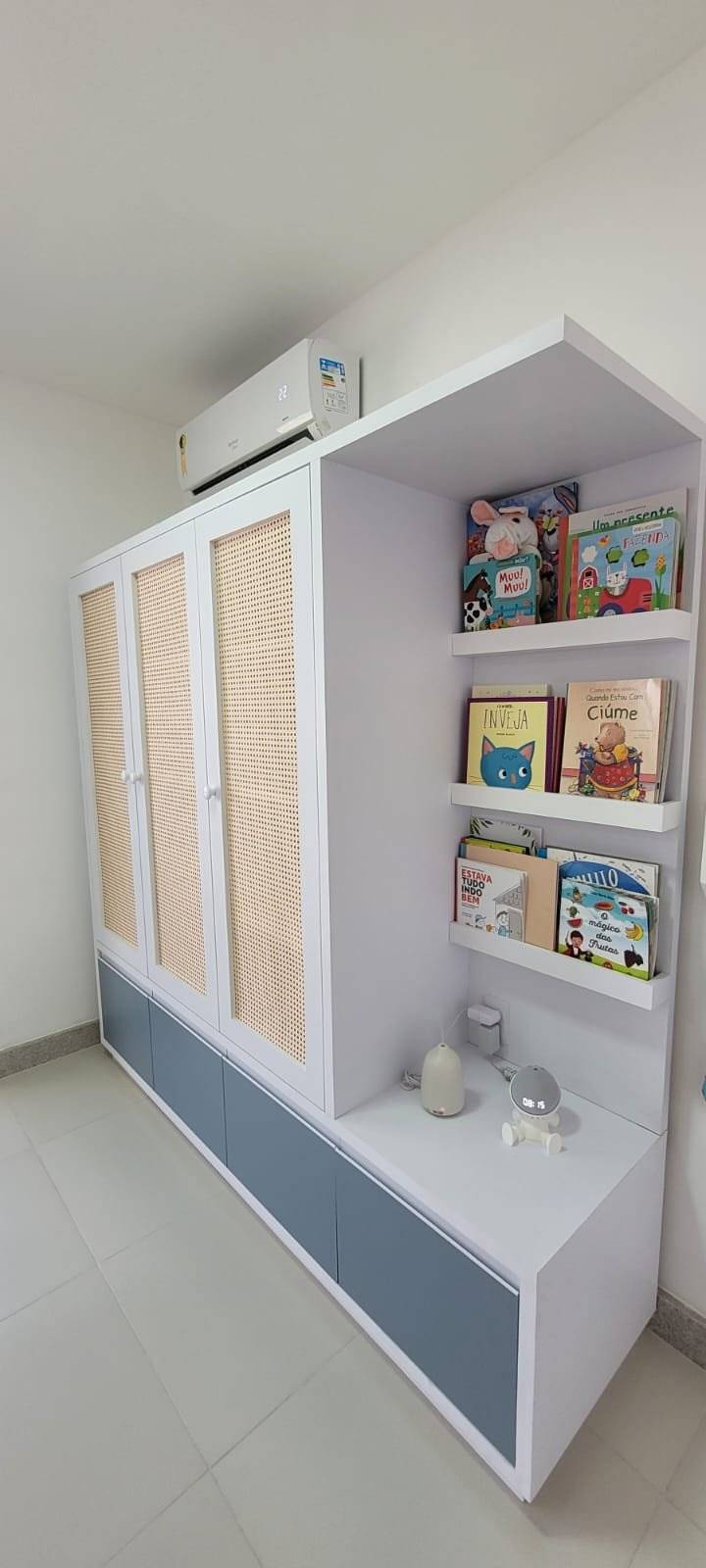 Armário branco com nichos de brinquedos e livros, ao lado de uma janela