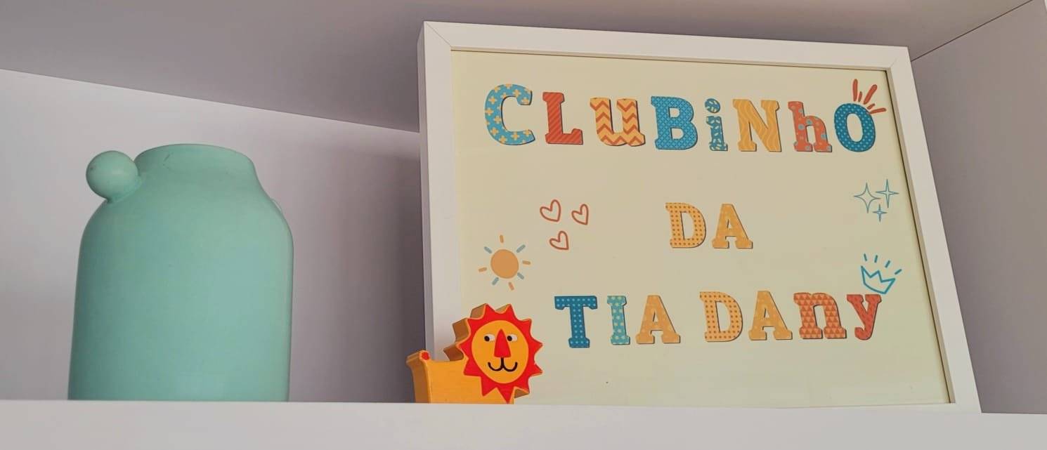 Quadro colorido escrito Clubinho da Tia Dany ao lado de um vaso verde-água